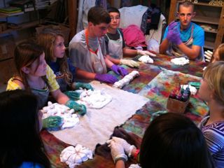 Awaiting Color A group of children sitting around a table with t-shirts prepared for tie-dye